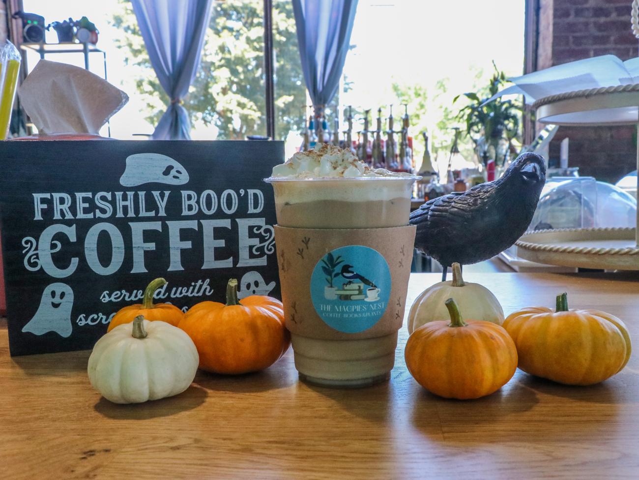 A spiced pumpkin drink in a Magpies' Nest cup with mini pumpkins and a crow figurine