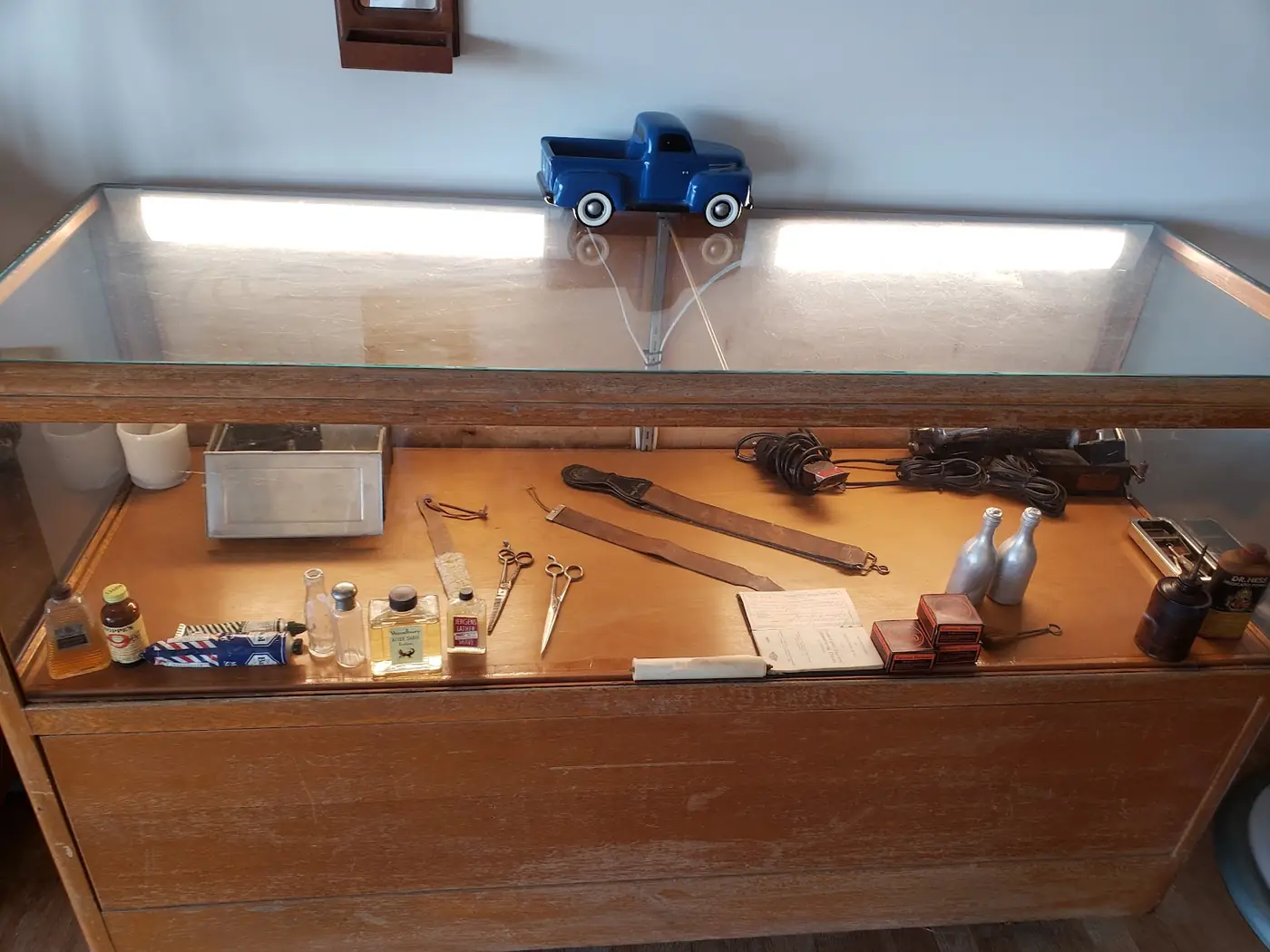 A glass case of antique straight razors, strops, clippers and tonics