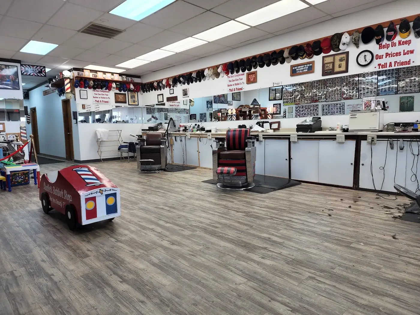 Inside Stadler's: a long bright room with vintage barber chairs, a rail of baseball caps and the red race car