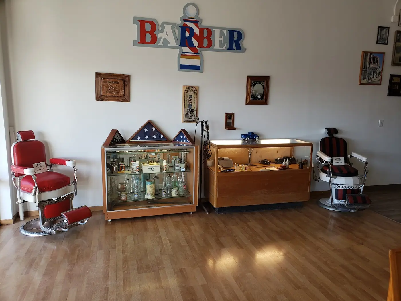 Two vintage porcelain barber chairs under a BARBER sign, with glass display cases